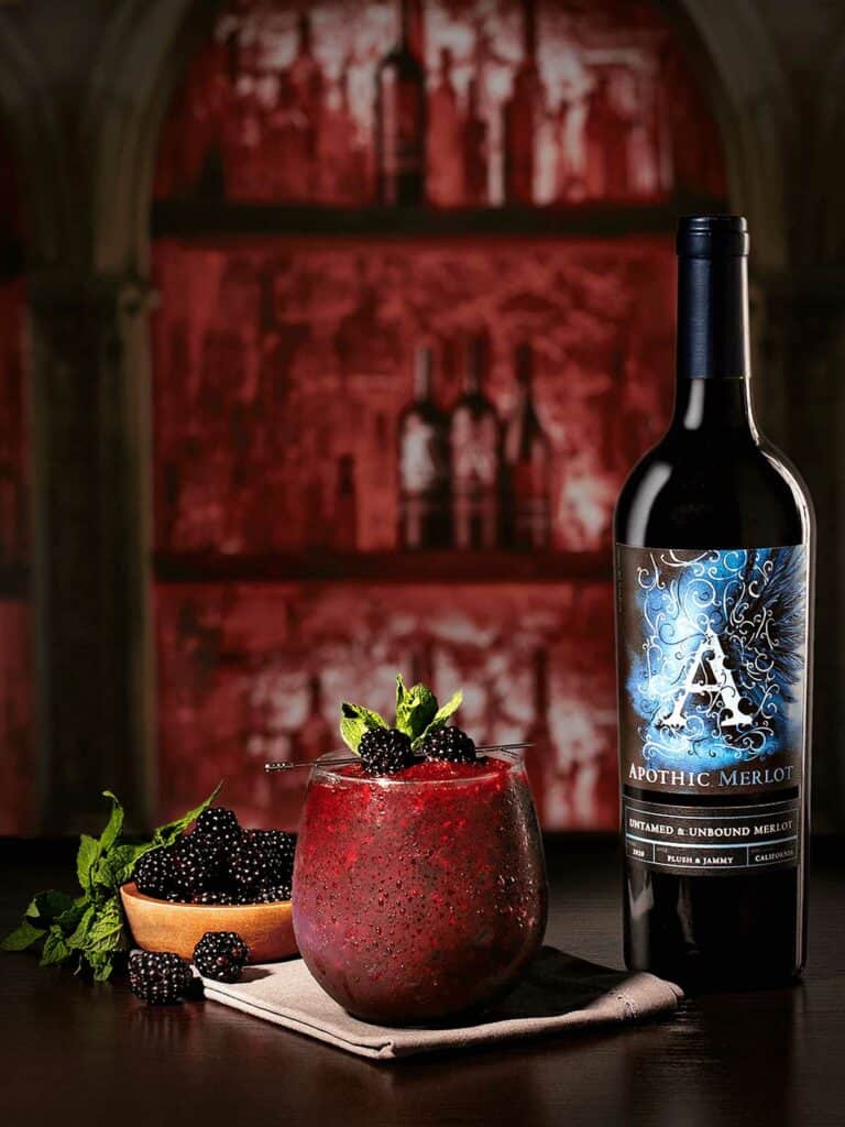 Un cocktail Apothic Black ice avec des bleuets et une bouteille de Merlot.
