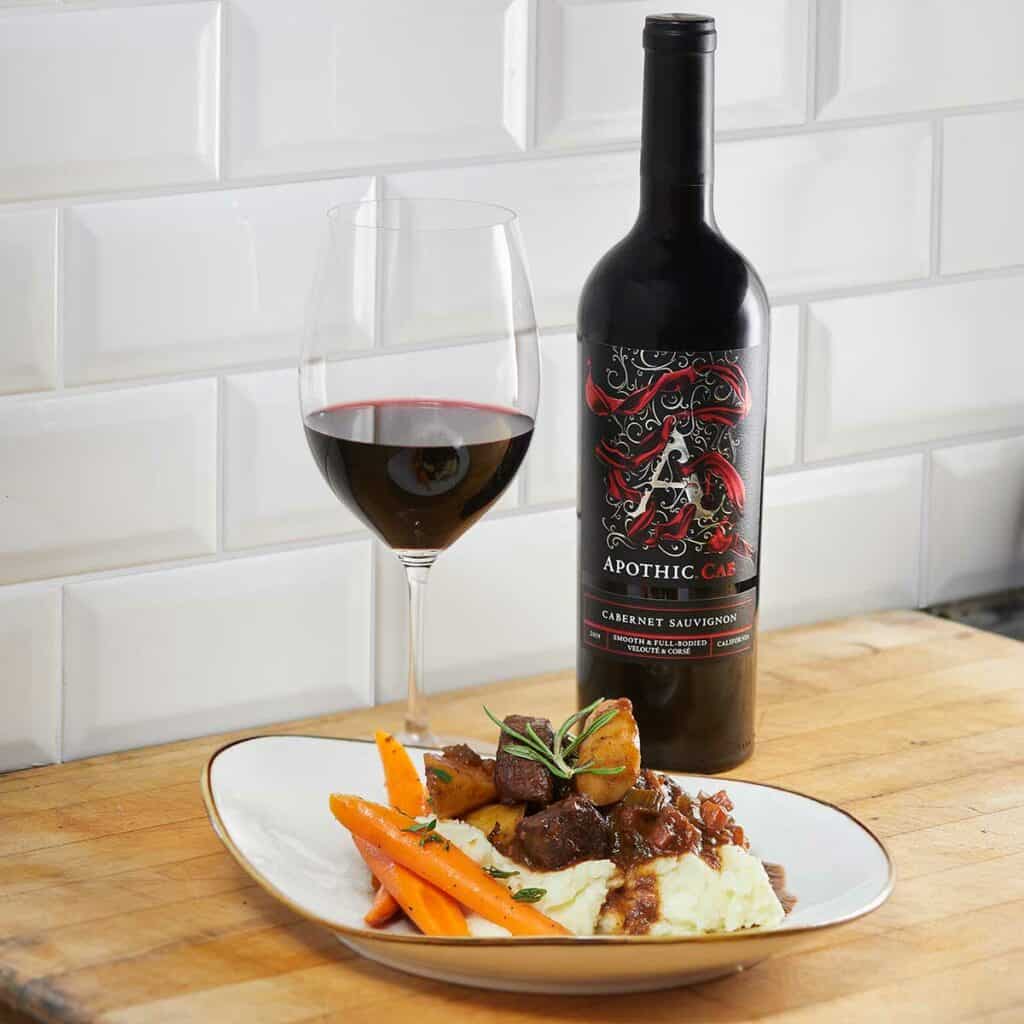 Braised beef plate in front of a glass and a bottle of Apothic Cab