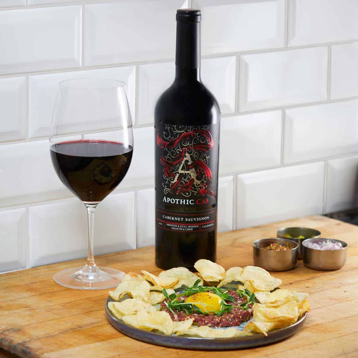 A beef tartare plate in front of a glass and a bottle of Apothic Cab
