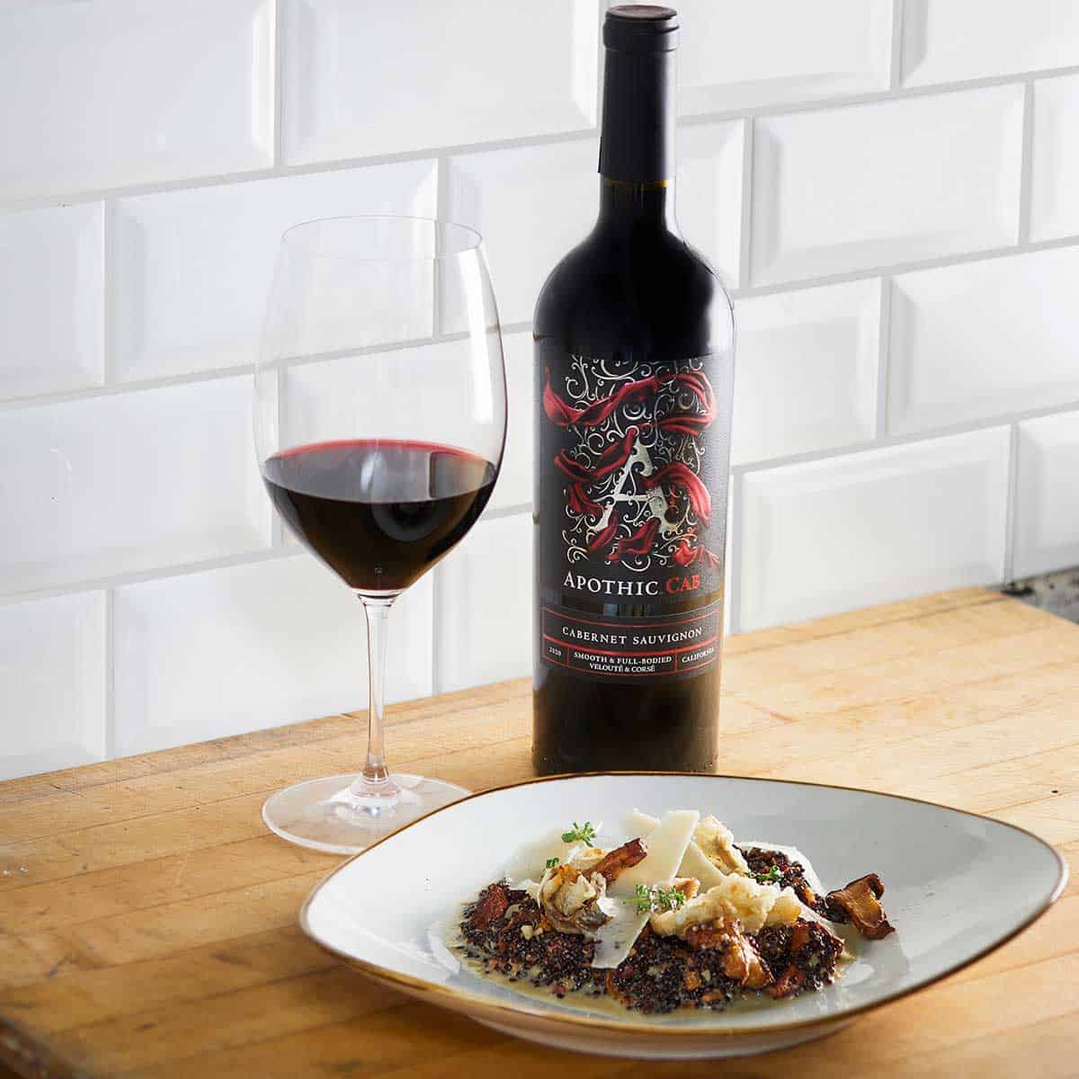 A quinoa risotto plate in front of a glass and a bottle of Apothic Cab