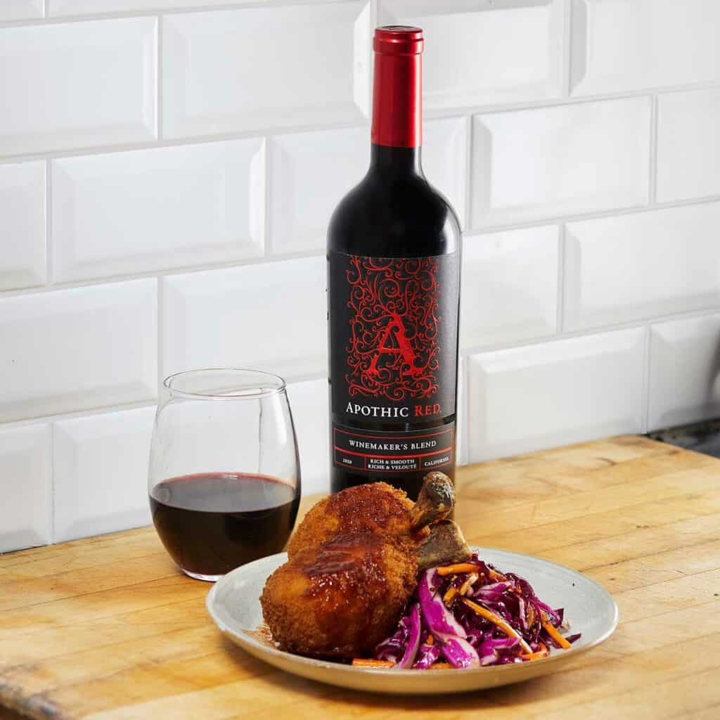 A fried chicken plate in front of a glass and a bottle of Apothic Red