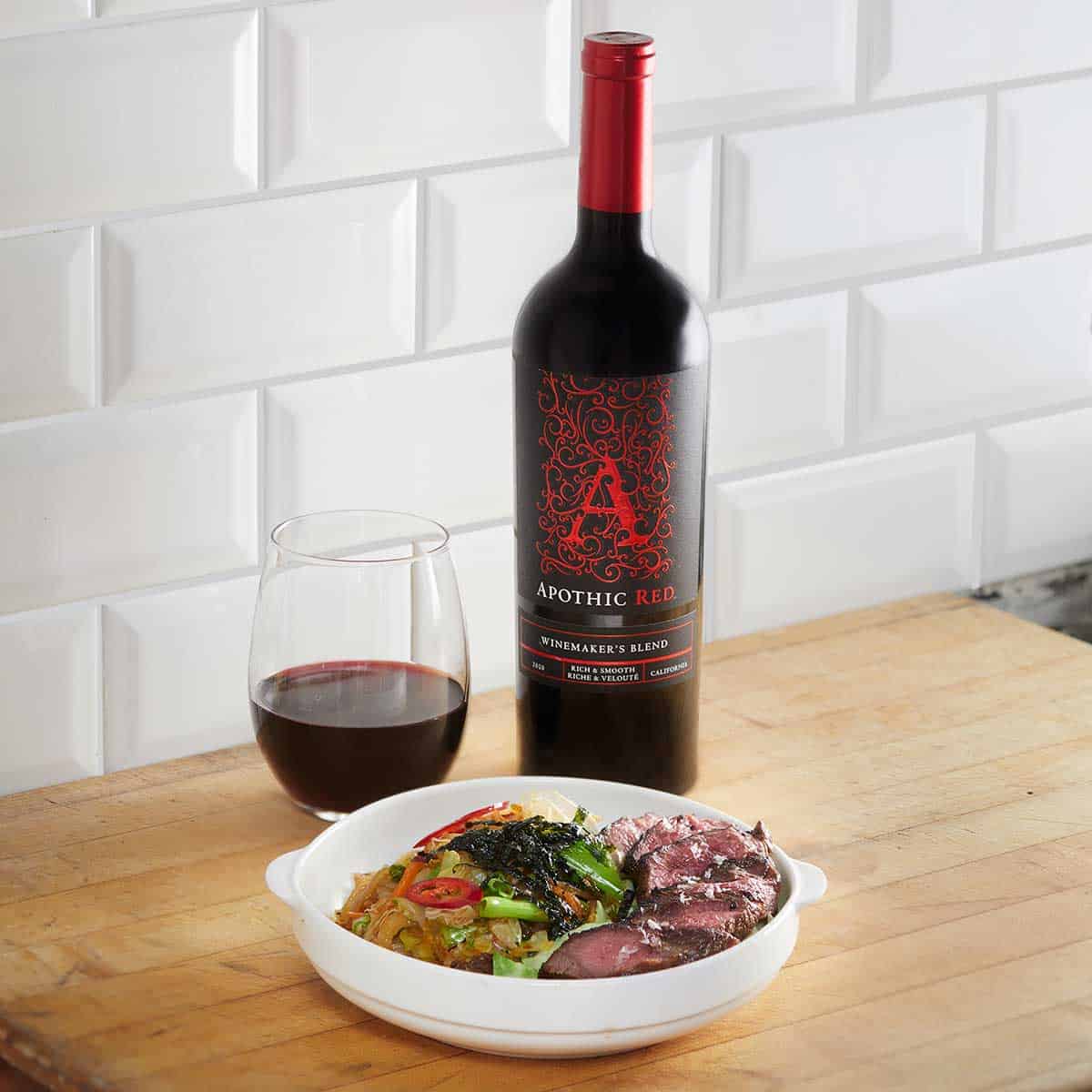 A yaki udon bowl in front of a glass and a bottle of Apothic Red