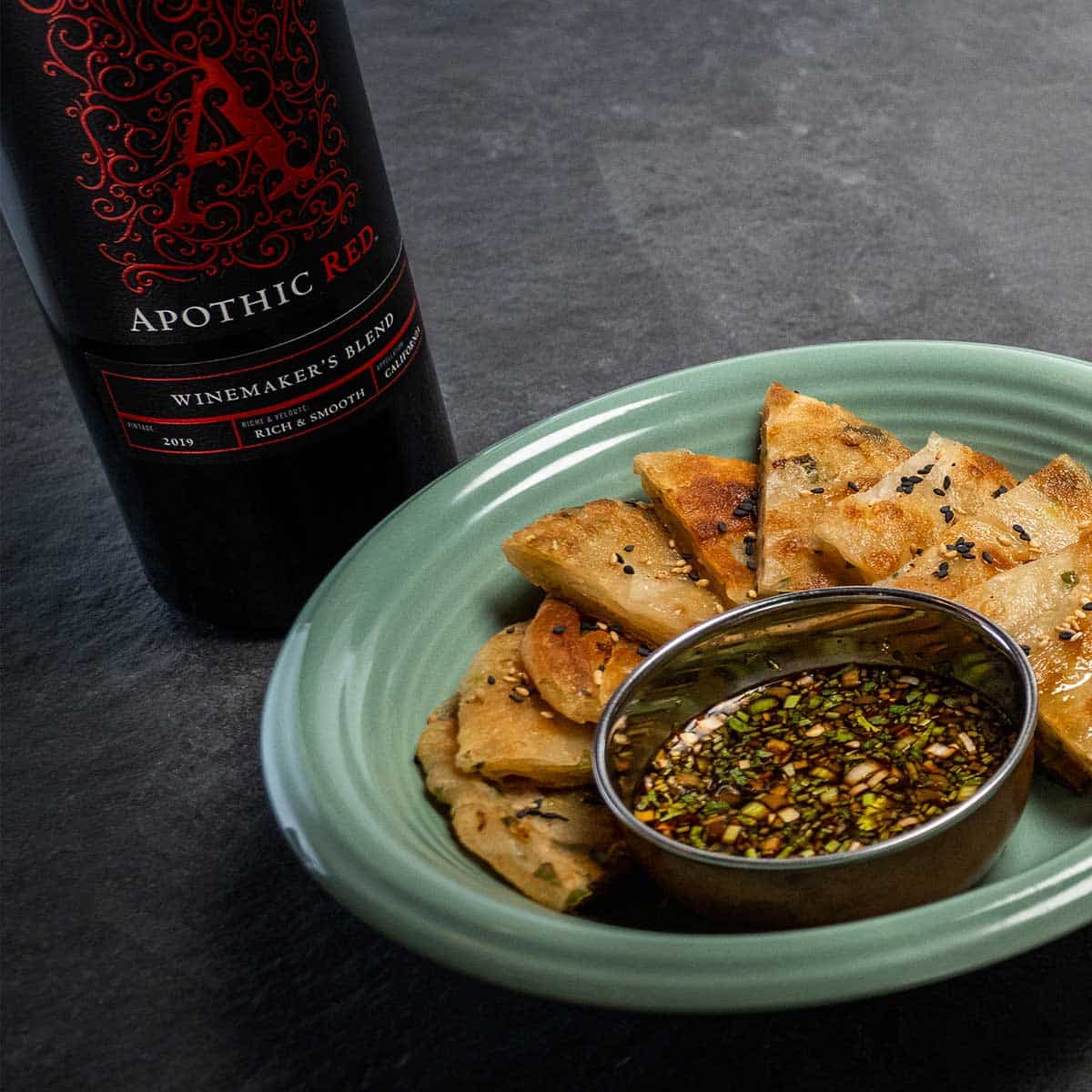 Plate of scallions pancakes with sauce and a bottle of Apothic red