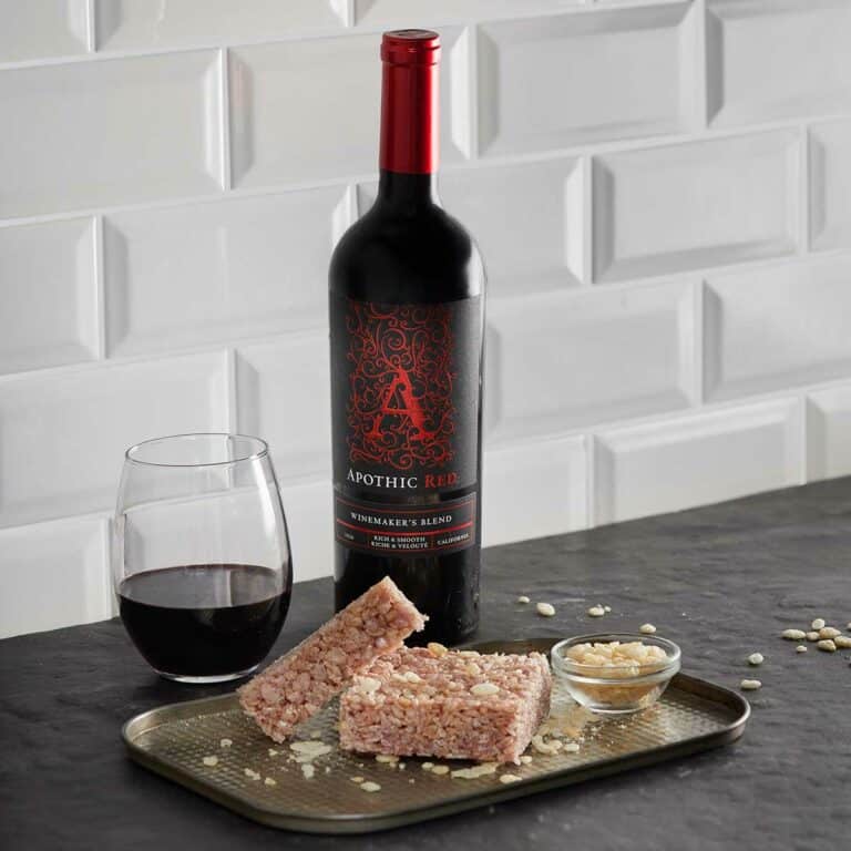 Red rice crispy square in a silver serving tray in front of a glass and a bottle of Apothic Red