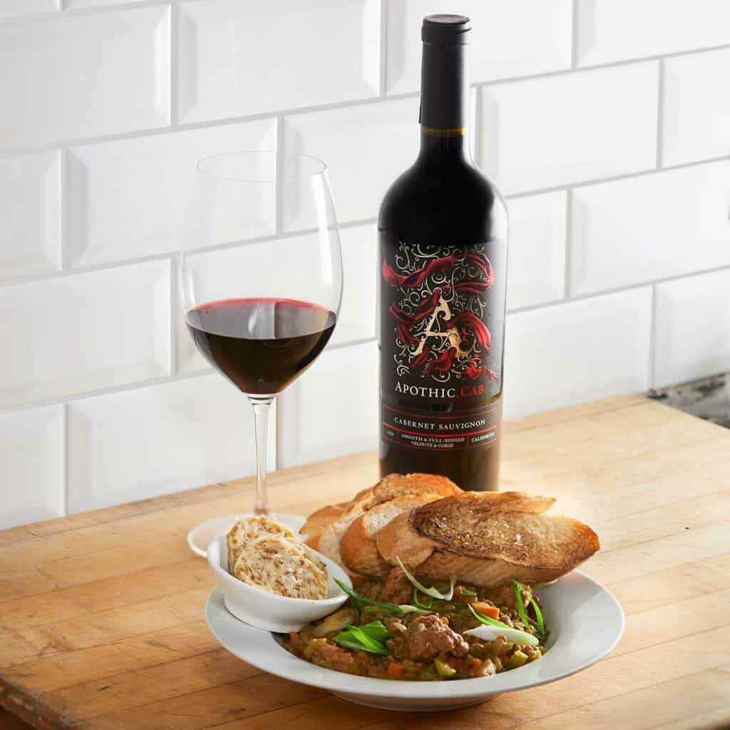 Lentil stew bowl with bread croutons in front of a glass and a bottle of Apothic Cab