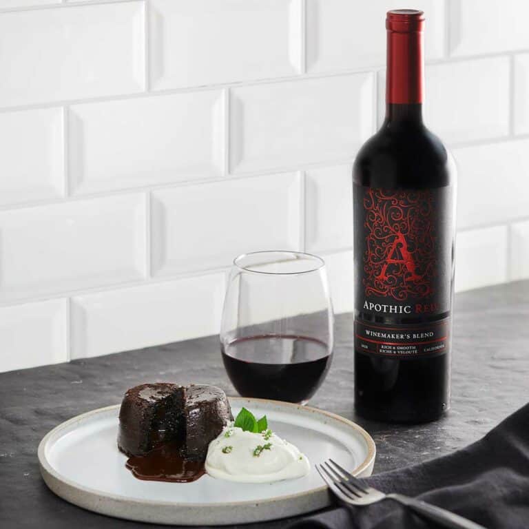 A chocolate lave cake in a plate in front of a glass and a bottle of Apothic Red