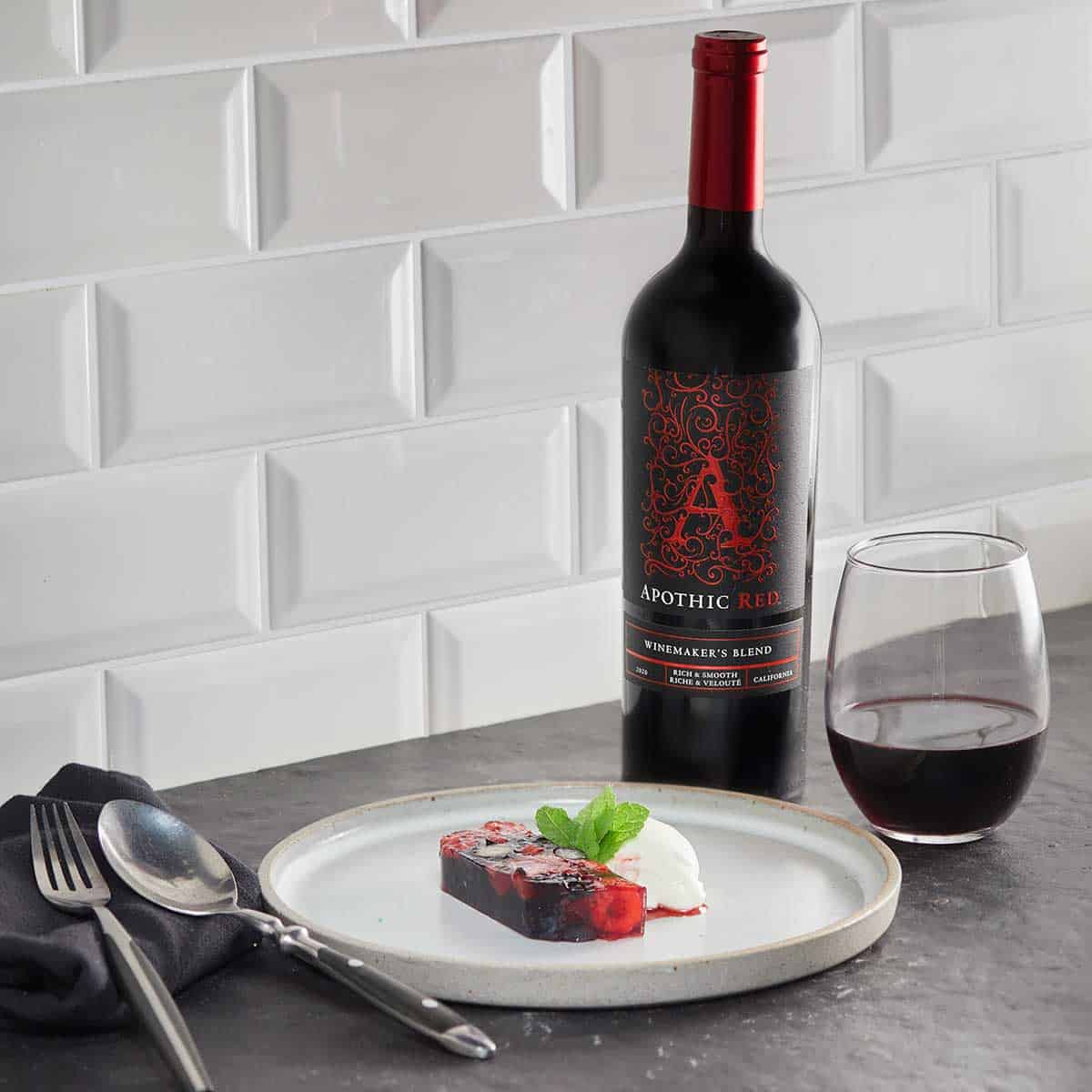 A fruits terrine in a plate in front of a glass and a bottle of Apothic Red