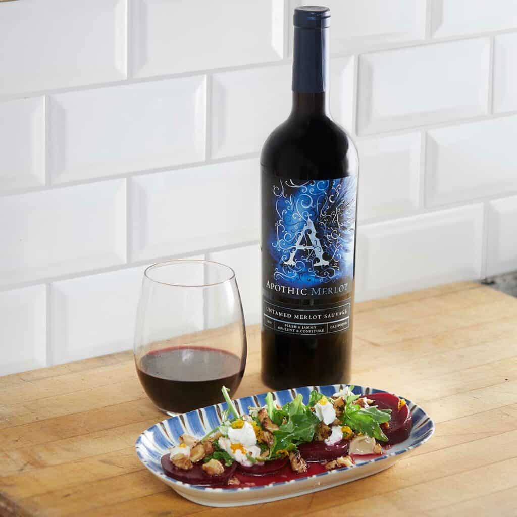 A toasted beet and walnut salad plate in front of a glass and a bottle of Apothic Merlot