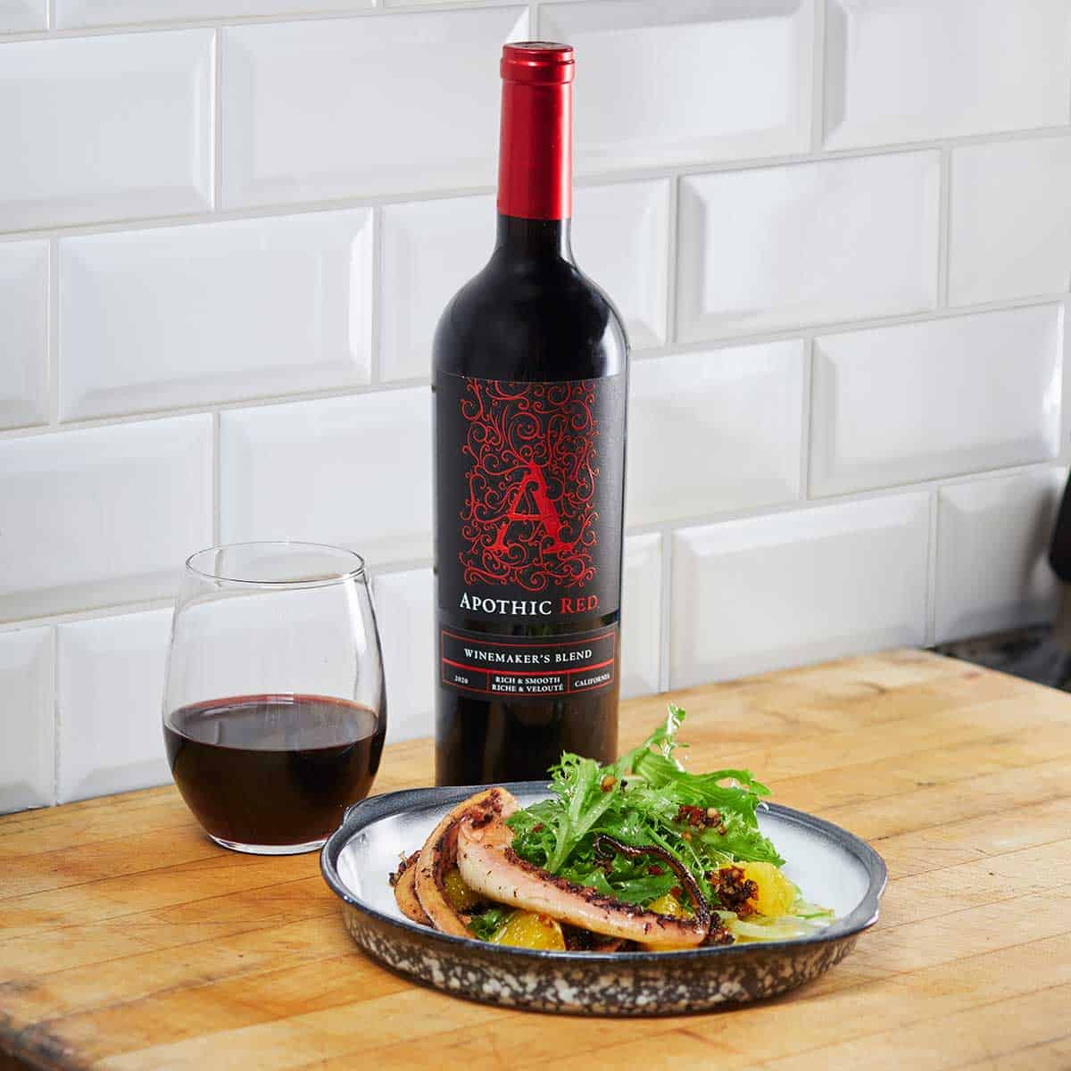 An octopus salad plate in front of a glass and a bottle of Apothic Red